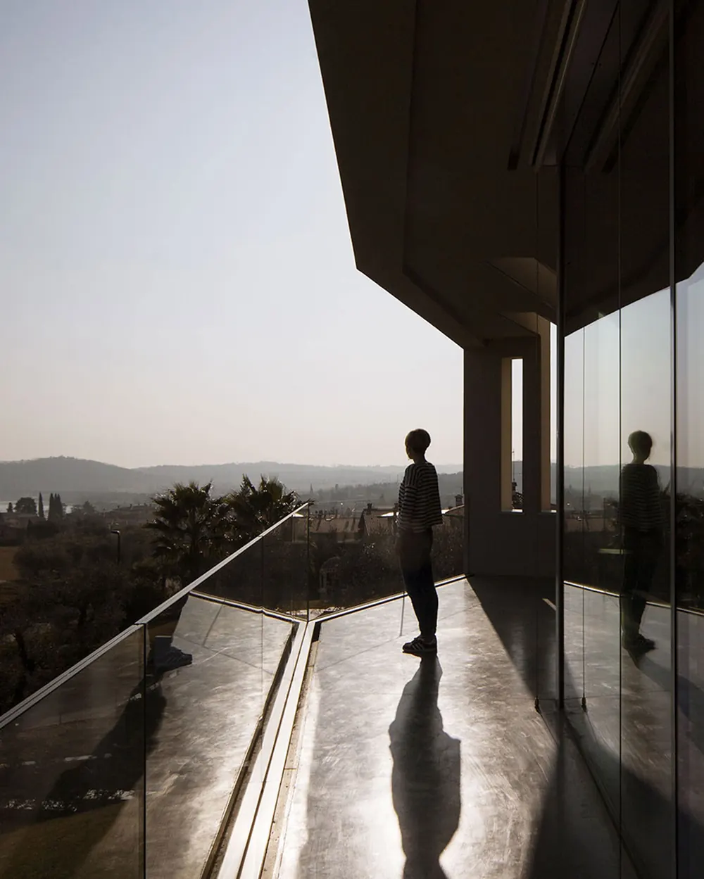 Atelier Rodighiero: persona sulla terrazza vetrata di una villa al tramonto