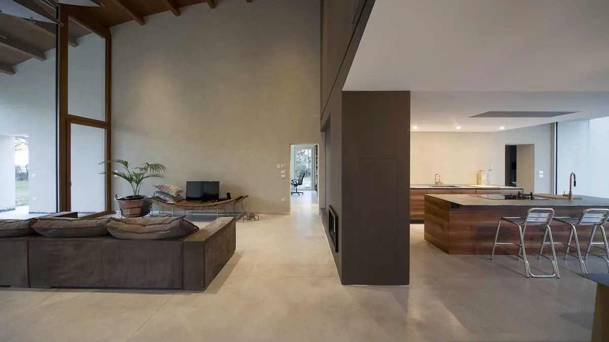 Villa in campagna: soggiorno a doppia altezza con travi in legno, divano e cucina con isola sullo sfondo