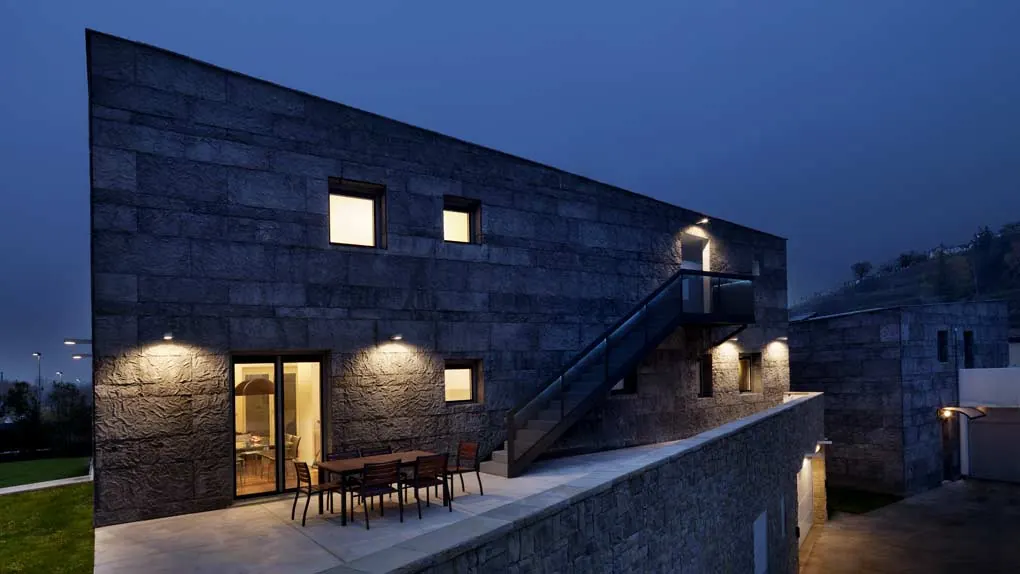 Villa rivestita in pietra di sera: terrazza con tavolo e scala esterna in metallo lungo la facciata