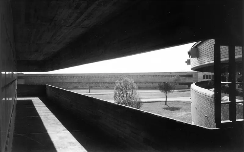 Cimitero di Castiglione delle Stiviere, fotografia in bianco e nero: lo sbalzo in calcestruzzo inquadra il paesaggio e un edificio basso