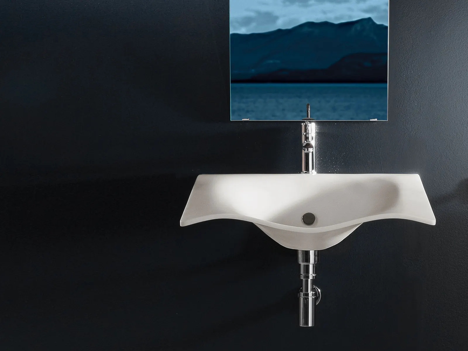Lavabo Flight: lastra sagomata bianca dalle linee sinuose, sospesa su parete scura sotto uno specchio