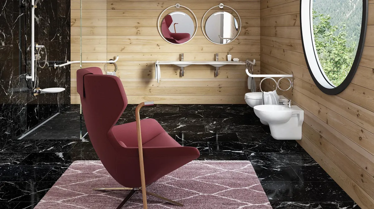 Serie Giotto in un bagno con pavimento e doccia in marmo nero e pareti in legno: sedile ribaltabile e maniglioni nella doccia, specchi tondi sopra i lavabi, una poltrona rossa in primo piano