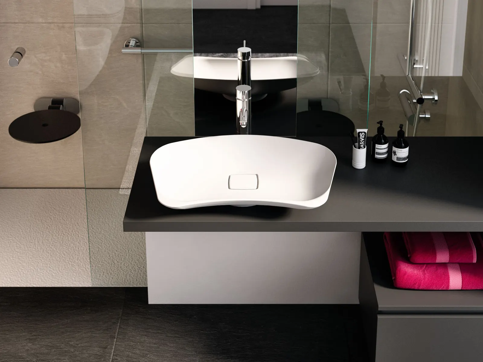 Lavabo d'appoggio Prime bianco su un piano scuro, con miscelatore cromato e specchio; a sinistra la doccia con un sedile ribaltabile tondo