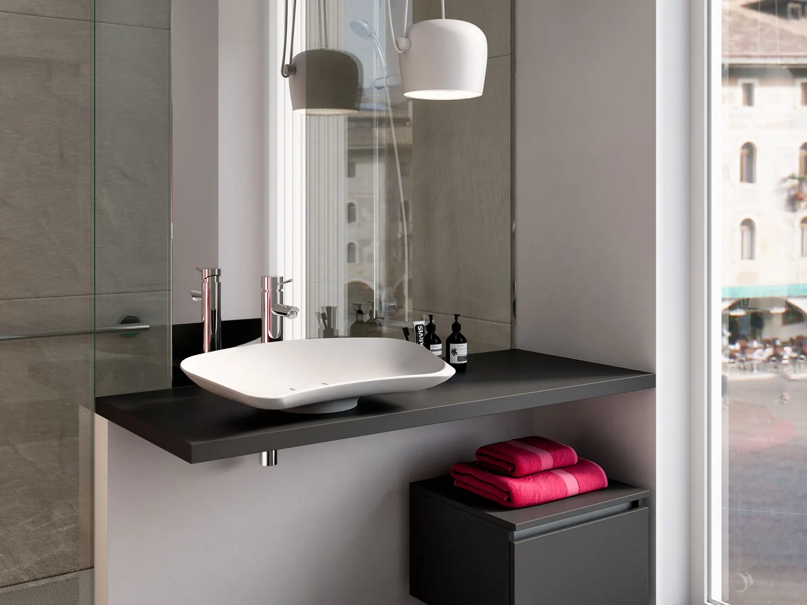 Lavabo Prime su piano scuro accanto a una finestra sulla città, con lampade a sospensione e asciugamani rossi