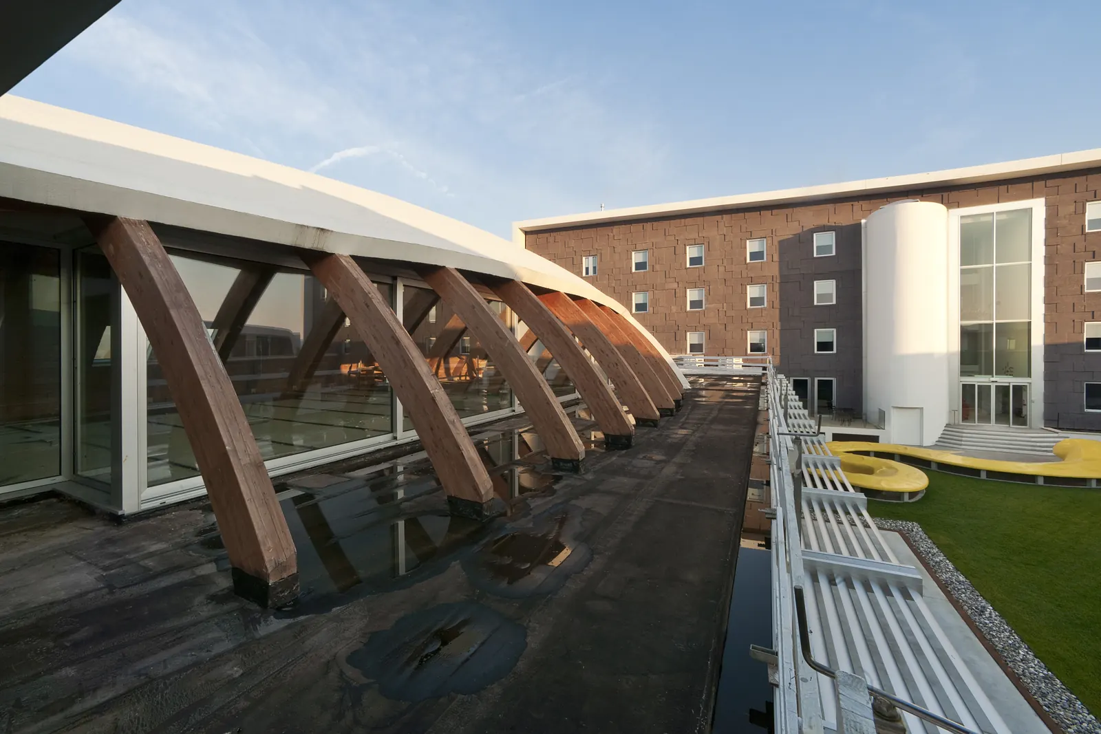 Hotel Dunant: travi lamellari curve della copertura del centro congressi e, oltre, la corte con il corpo dell'albergo a pannelli bruni e il volume cilindrico delle scale