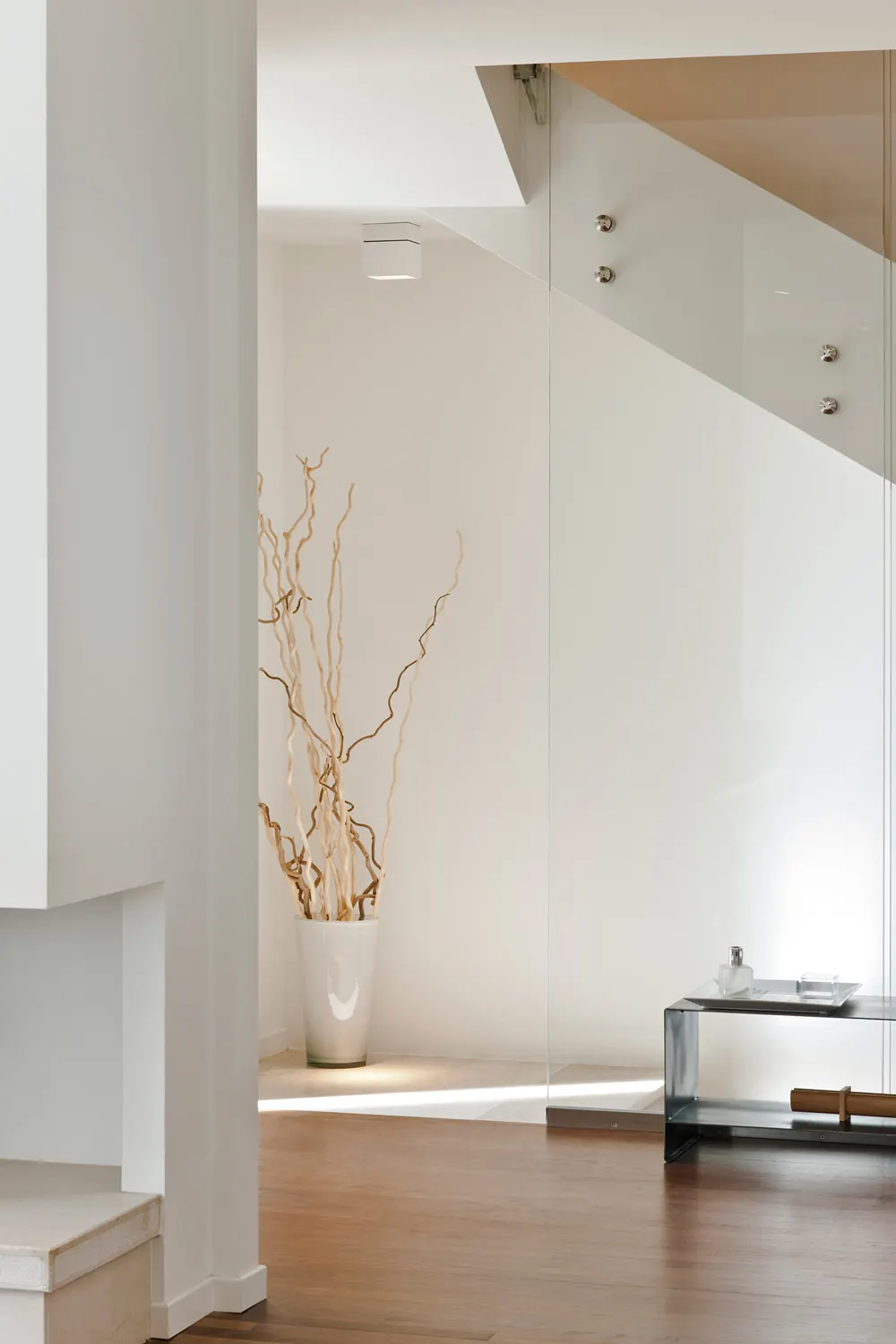 Interno residenziale bianco con scala sospesa e luce naturale radente