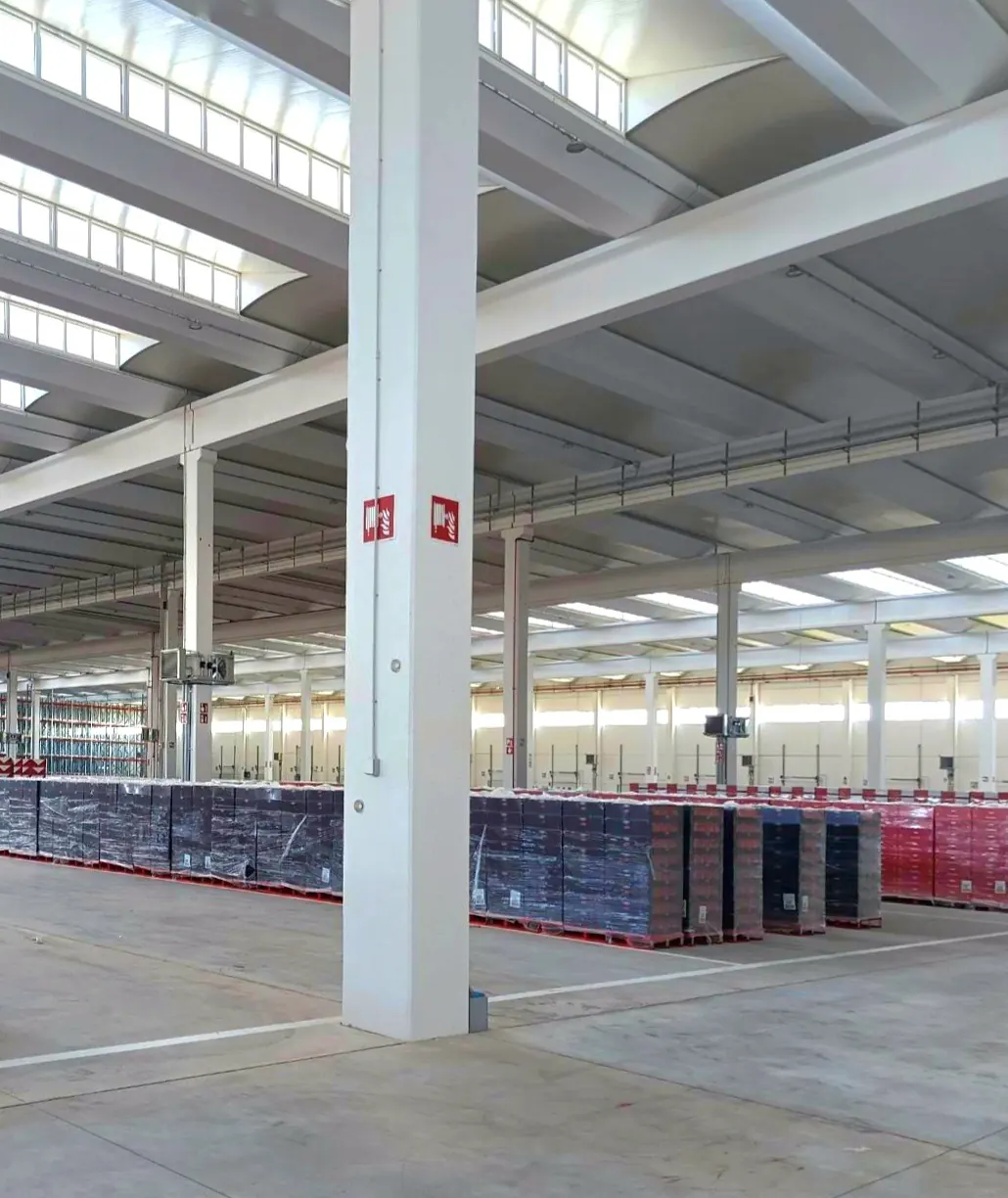 Interno del magazzino: pilastri in calcestruzzo, travi di copertura con i lucernari e le merci pallettizzate